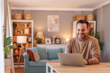 Portrait of businessman smiling and analyzing data over laptop while working at desk in home office