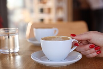 Woman with cup of aromatic coffee at wooden table in cafe, closeup