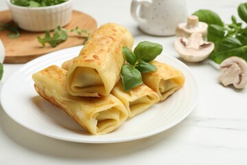 Delicious rolled crepes with basil and mushrooms on white marble table, closeup
