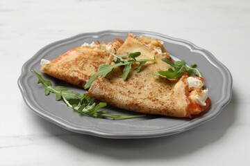 Delicious crepes with salmon, cream cheese and arugula on white marble table, closeup