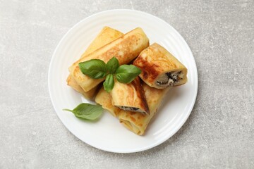 Delicious rolled crepes with mushrooms and basil on grey table, top view