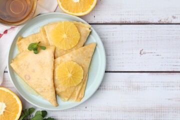 Delicious Crepes Suzette, tea and oranges on white wooden table, flat lay. Space for text