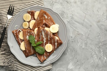 Delicious chocolate crepes with banana, condensed milk and mint served on grey table, top view. Space for text