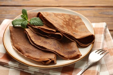 Delicious chocolate crepes and mint on wooden table, closeup