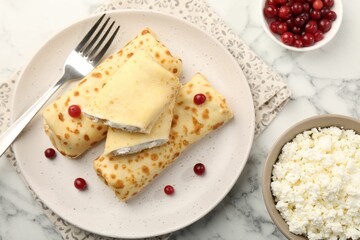 Delicious rolled crepes with cottage cheese, raisins and cranberries on white marble table, flat lay