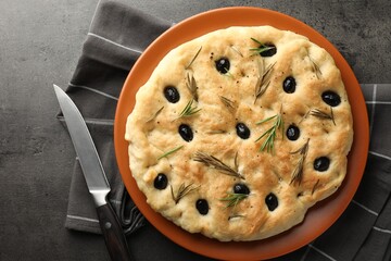 Delicious focaccia bread with olives, rosemary and knife on grey table, top view