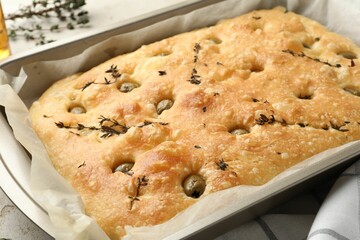 Delicious focaccia bread with olives and thyme in baking dish on table, closeup