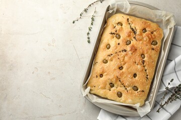 Delicious focaccia bread with olives and thyme in baking dish on light grey table, top view. Space for text