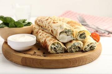 Tasty rolled crepes with cottage cheese and spinach served on white wooden table, closeup