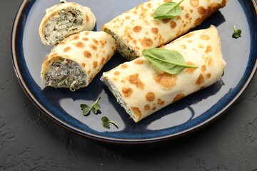 Delicious crepes with cottage cheese and spinach on black table, closeup