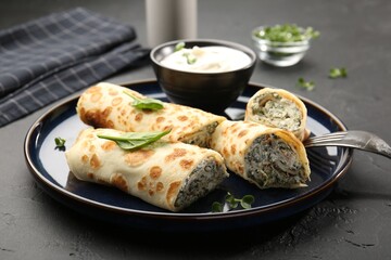 Delicious crepes with cottage cheese, spinach and sour cream served on black table, closeup