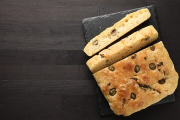 Pieces of delicious focaccia bread with olives and thyme on dark wooden table, top view. Space for text