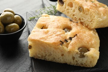 Pieces of delicious focaccia bread with olives and thyme on black table, closeup