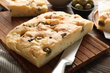 Pieces of delicious focaccia bread with olives, thyme, salt and knife on wooden table, closeup