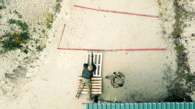 Aerial View of Tactical Shooting Training. Overhead shot of two soldiers practicing shooting on a sandy range, one prone with a rifle, highlighting military training.