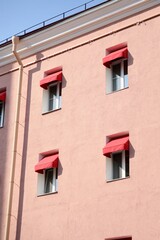 classic-style historic pink house with red awnings on windows. sunny day. stylish architecture in center of metropolis. hotel or apartment building