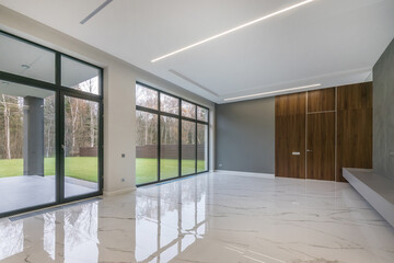 A spacious, bright hall in a country house with panoramic windows and a view of a green lawn and an autumn forest. Unfurnished.