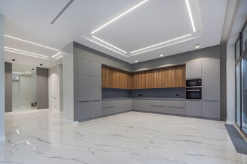 A room in a country house with a modern design. White tiled floor, panoramic window and installed gray kitchen set. Unfurnished.