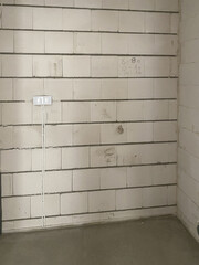 Empty brick wall with two electrical sockets, flat in the process of renovation from the builder, floor with concrete screed 