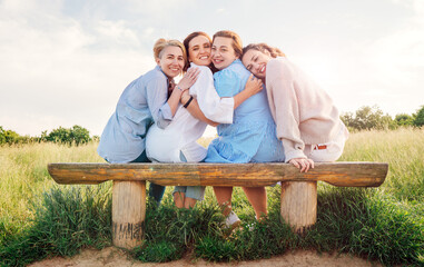 Four smiling women dressed light summer clothes harm embracing sitting on meadow bench during...