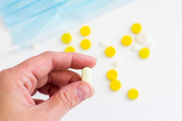 yellow and white pills in hand with a medical mask on a white background