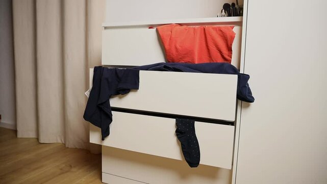 open drawers of a white chest of drawers from which various items of clothing hang. the concept of putting things in order, organizing space, minimalism, as well as in advertising campaigns for storag