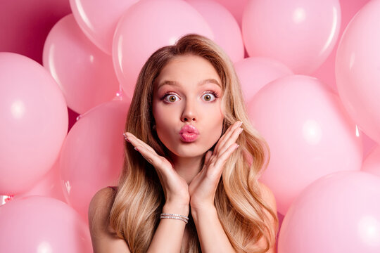 Charming young woman posing with kissy face in front of pink balloons, exuding glamour and style