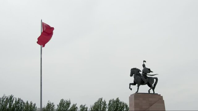 Establishing shot of Bishkek, Kyrgyzstan with the flag of Kyrgyzstan waving in front of the statue of Manas in Ala Too Square.