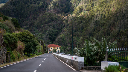 A scenic rural road leading to a house with a red roof, surrounded by lush green hills and dense...