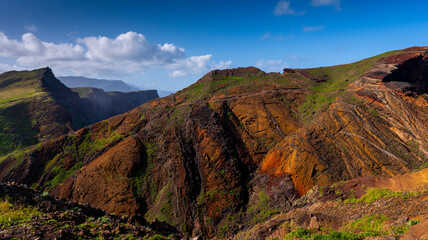 A vibrant mountain landscape with rugged cliffs and colorful rock formations covered in patches of greenery under a bright blue sky. A breathtaking view of natural beauty.