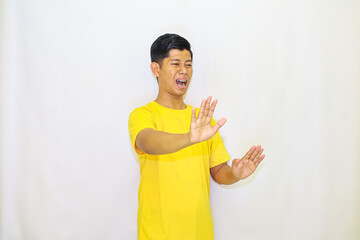 A man in a yellow shirt expresses disgust and rejection with raised hands against a white background, showing an obvious dislike for something,