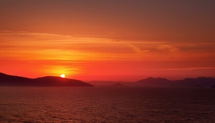 Fiery sunset over tranquil ocean and silhouetted mountains.