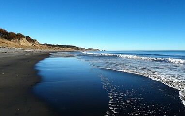 Tranquil black sand beach with ocean waves under a clear blue sky.