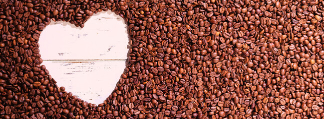 A heart shape crafted from rich brown coffee beans is artistically arranged on a rustic wooden...
