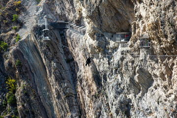 A girl on a zipline descends between the rocks above a canyon in the mountains