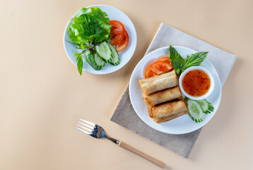 Fried spring rolls, vegetables and tomatoes arranged  on an orange table with dipping sauce.