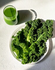 Top view of green kale juice smoothie and fresh kale leaves in a white plate on white background