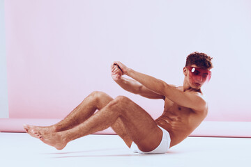 Obraz premium Confident young man in pink sunglasses posed on the floor in minimalistic studio with soft pastel background. Fashion and style concept emphasizing self-expression.