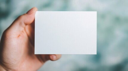 Person presenting a blank white business card with a soft blurred background, showcasing the card's potential for customization and personal branding