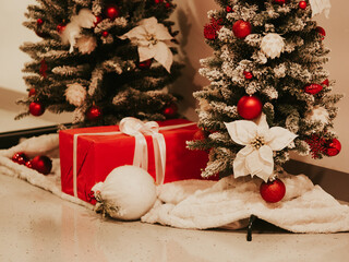 Red gift box tied with white satin ribbon. Present under tree. Christmas tree decorations on branches of Artificial Christmas tree. New Year celebration concept. December 31, 2024 - Pula, Croatia