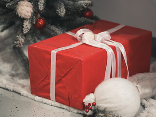 Red gift box tied with white satin ribbon. Present under tree. Christmas tree decorations on branches of Artificial Christmas tree. New Year celebration concept. December 31, 2024 - Pula, Croatia