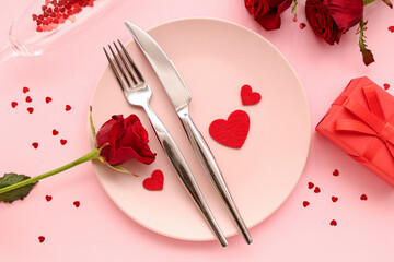 Beautiful table setting with red roses, gift box and hearts on pink background. Valentine's Day celebration