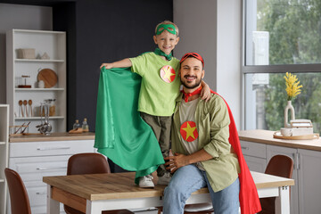 Happy father with his little son dressed as superheroes in kitchen at home