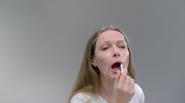Close-up portrait of Old woman uses lipstick or a pomade. Senior female applies make up or cosmetics to the lips. Facial skin care in old age. Mature elderly lady. Concept of natural beauty.