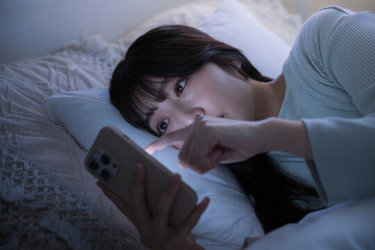 夜中にスマホを見て睡眠が足りず寝不足になってしまう女性のクローズアップでタップする　青色系