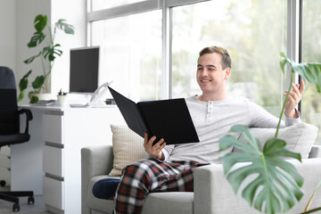 Young businessman with folder sitting on sofa in office. National Wear Your Pajamas to Work Day