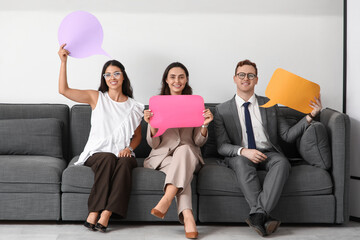 Business people with blank speech bubbles sitting on sofa in office