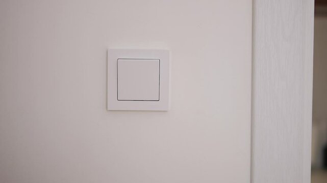 Womans hand turning light on and off using wall switch Simple control of light enhances room's atmosphere Concept of energy-saving modern home lighting and daily interaction with light systems