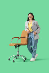 Young businesswoman with folder and office chair on green background