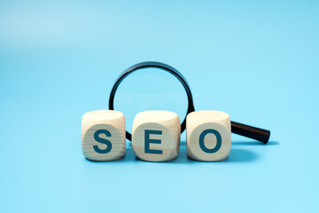SEO, Search Engine Optimization text wooden cube blocks with a magnifying glass on blue background,...